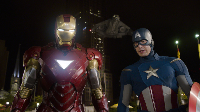 Robert Downey Jr. as Iron Man standing next to Chris Evans as Captain America as they look down at Loki in The Avengers