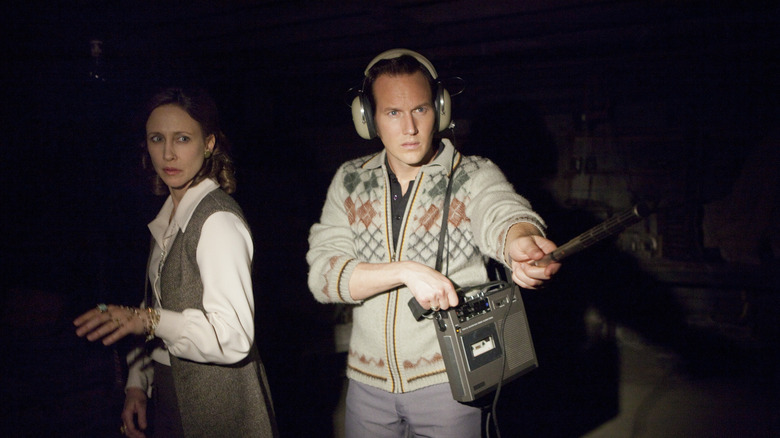 Vera Farmiga as Lorraine Warren and Patrick Wilson as Ed Warren in The Conjuring, lit by the light from the camera as they investigate a case, as Ed is equipped with headphones and recording gear.