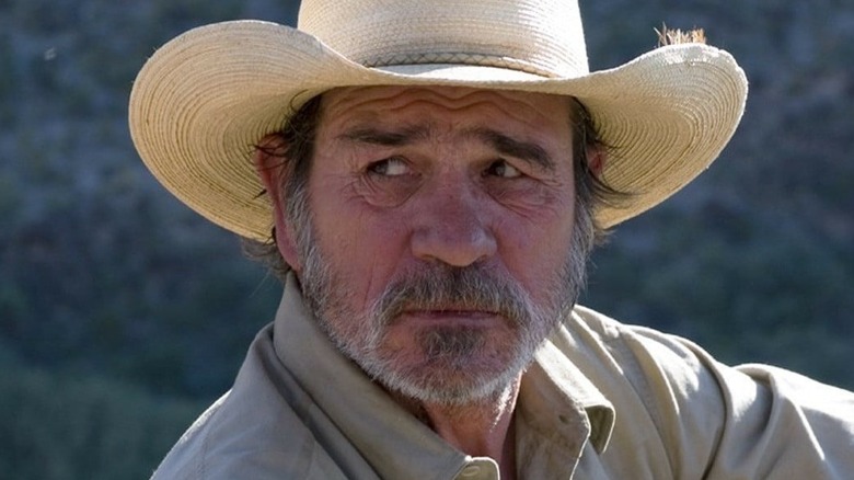 Tommy Lee Jones as Pete Perkins in The Three Burials of Melquiades Estrada, sitting against a rock in his Western wear.