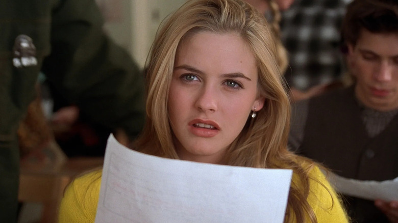 Alicia Silverstone as Cher Horowitz in Clueless, looking up from a paper with a puzzled expression.