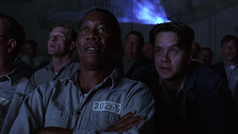 Tim Robbins as Andy Dufresne and Morgan Freeman as Ellis Boyd "Red" Redding in The Shawshank Redemption, the pair watching a movie with a crowd of other inmates in the prison's movie room.