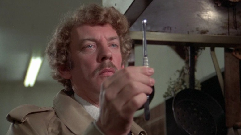 Donald Sutherland as Matthew Bennell in Invasion of the Body Snatchers, holding and looking at a metal device in his hands.