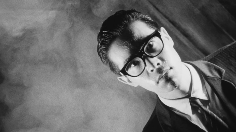 Tomorowo Taguchi as the Salaryman in Tetsuo: The Iron Man, seen at an extreme canted angle as he looks intensely at the camera with a background of smoke.