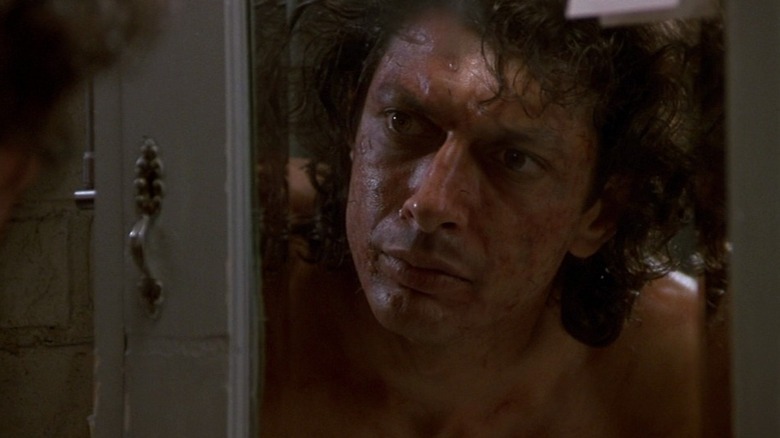 Jeff Goldblum as Seth Brundle in The Fly, observing his scab-ridden face in a mirror.
