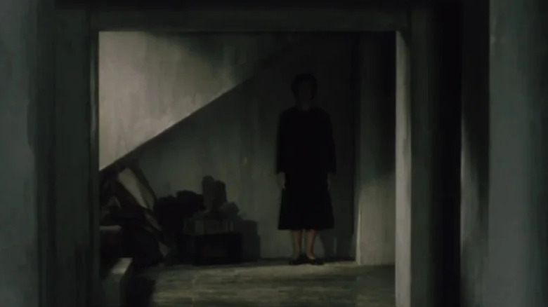 A ghostly woman stands in the shadows under a staircase in Pulse (2001)
