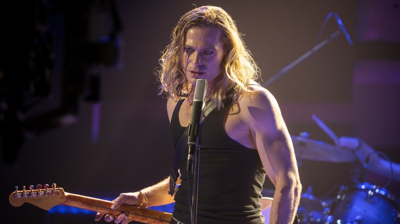Sam Reid as Lestat holding a guitar on a stage in The Vampire Lestat