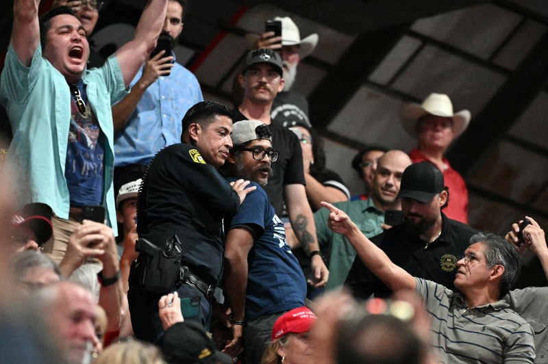 A protester is detained by a Sheriff deputy as US President Donald Trump speaks during a campaign rally at the Freeman Coliseum in San Antonio, Texas, on October 7, 2026. Republican Senate candidate Ken Paxton is in a close race with Democratic candidate James Talarico for one of Texas' US Senate seats. (Photo by Mandel NGAN / AFP via Getty Images)